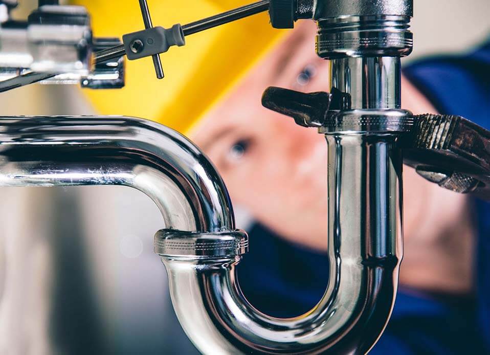 Skilled plumber inspecting exposed piping connections with diagnostic tools and flashlight