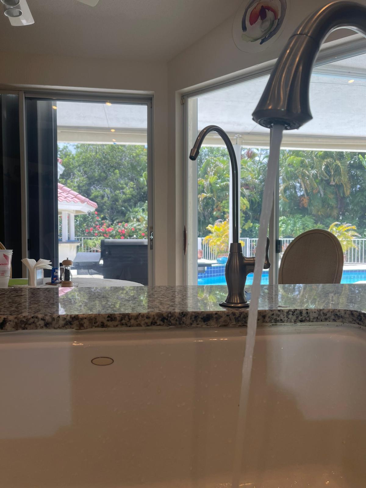 Modern kitchen sink with a tall chrome faucet overlooking a bright dining area and backyard.